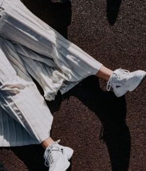 Une personne en jupe blanche plissée et baskets blanches allongée au sol